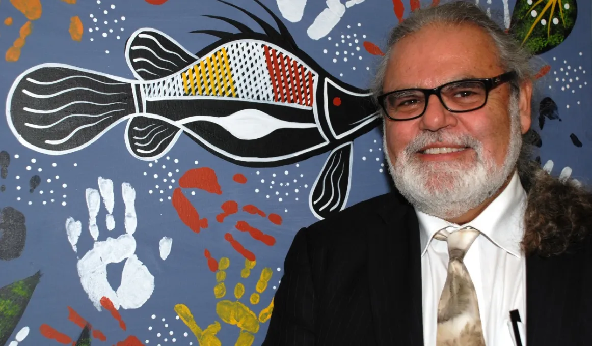 Founder & CEO of Nallawilli Technology, Roderick McLeod, stands in front of an indigenous painting