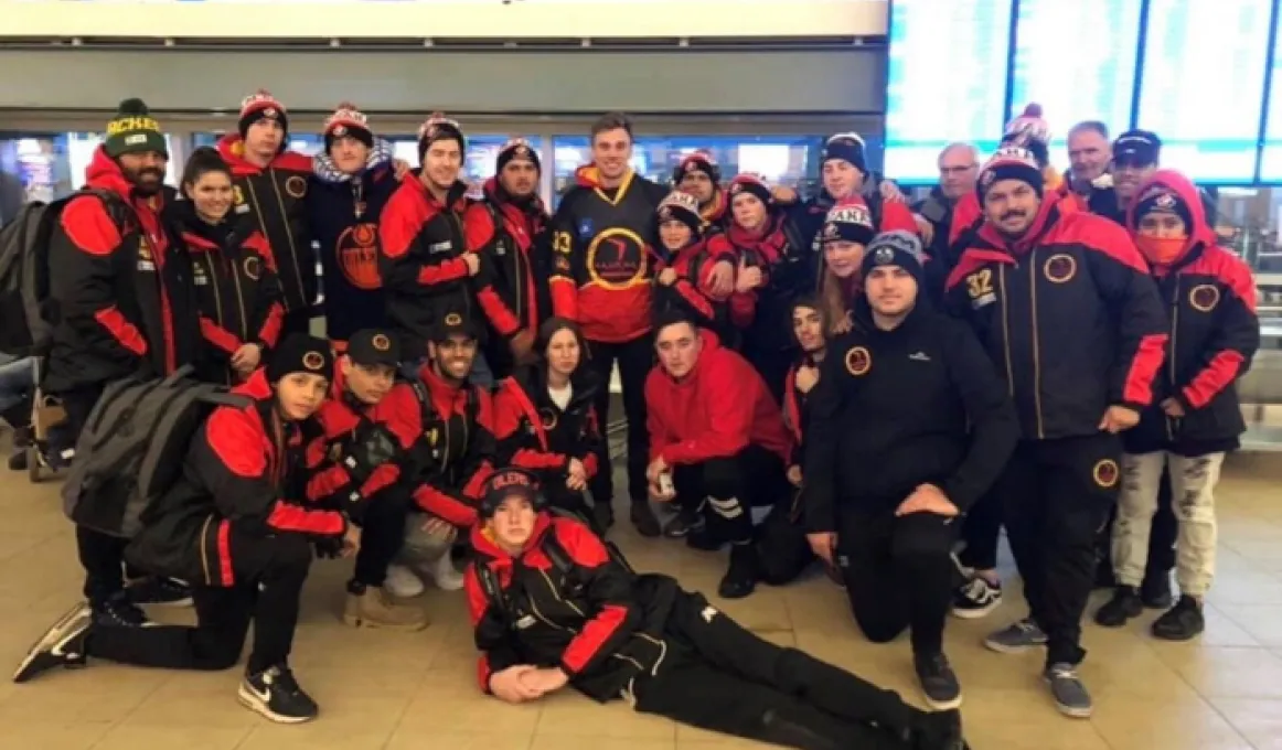 Image Alt text (for vision impaired readers) A team of young Indigenous men and women wearing red and black jackets, black pants and red and black hats.