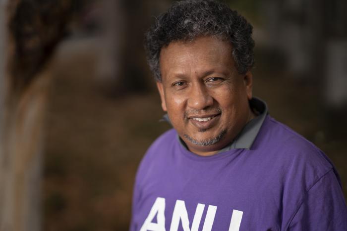 Aboriginal man with curly dark hair wearing a purple top with the letters A.N.U. on the front.