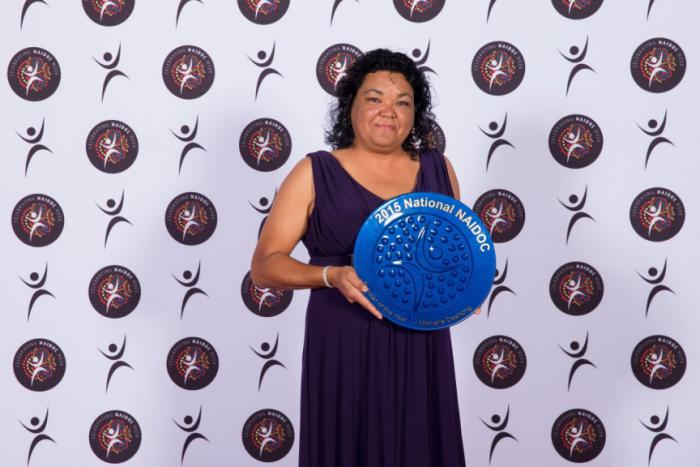 Indigenous woman Michelle Deshong holding blue plate shaped award.